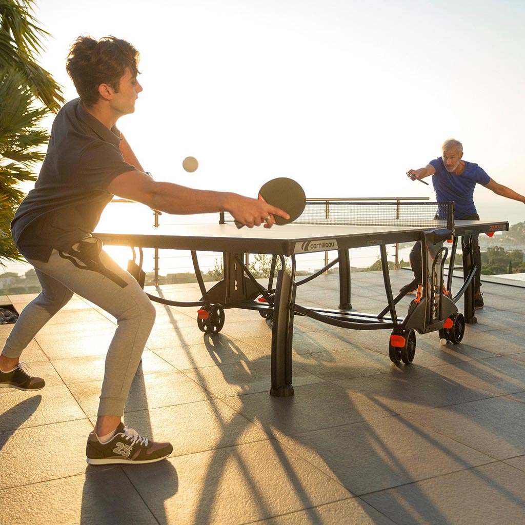 Two men playing a game of table tennis on a cornilleau table outdoors