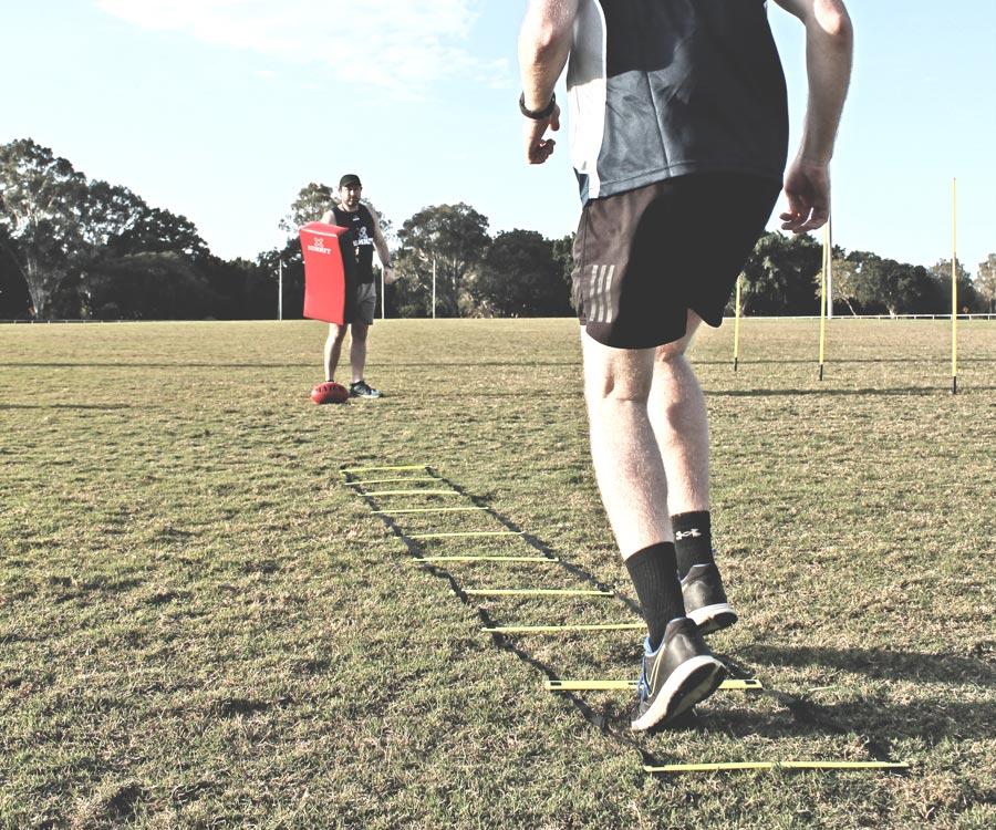AFL agility drill for the advanced players. AFL player training with agility hurdle while team-mate is ready with tackle bag. 