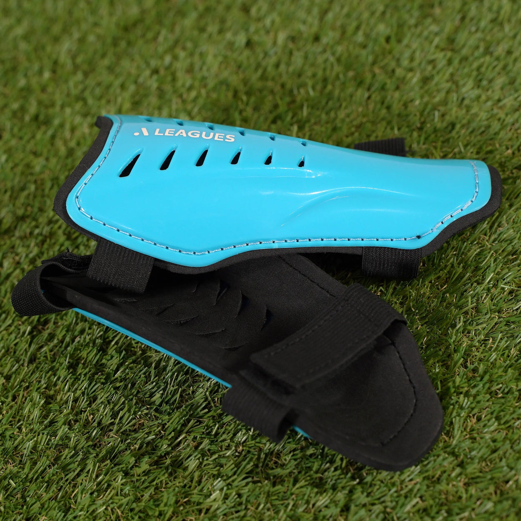 Blue shin guard with black straps on a grass background