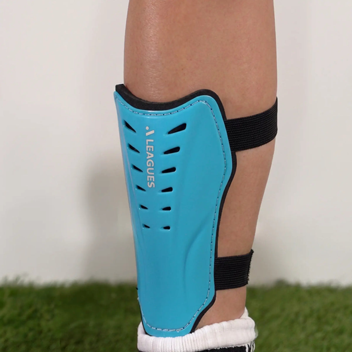 Blue shin guard with black straps on a childs leg, on a grassy surface.