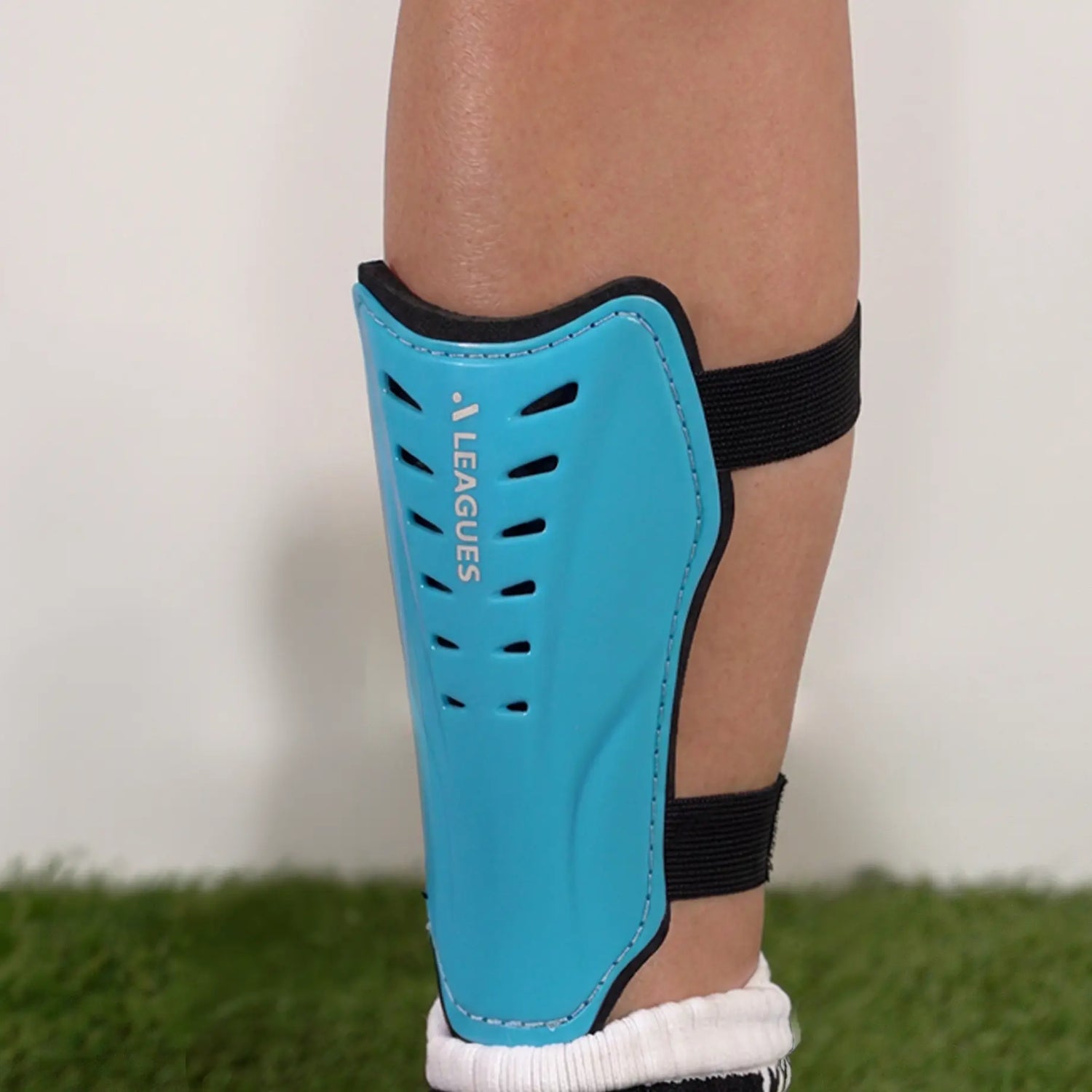 Blue shin guard with black straps on a childs leg, on a grassy surface.