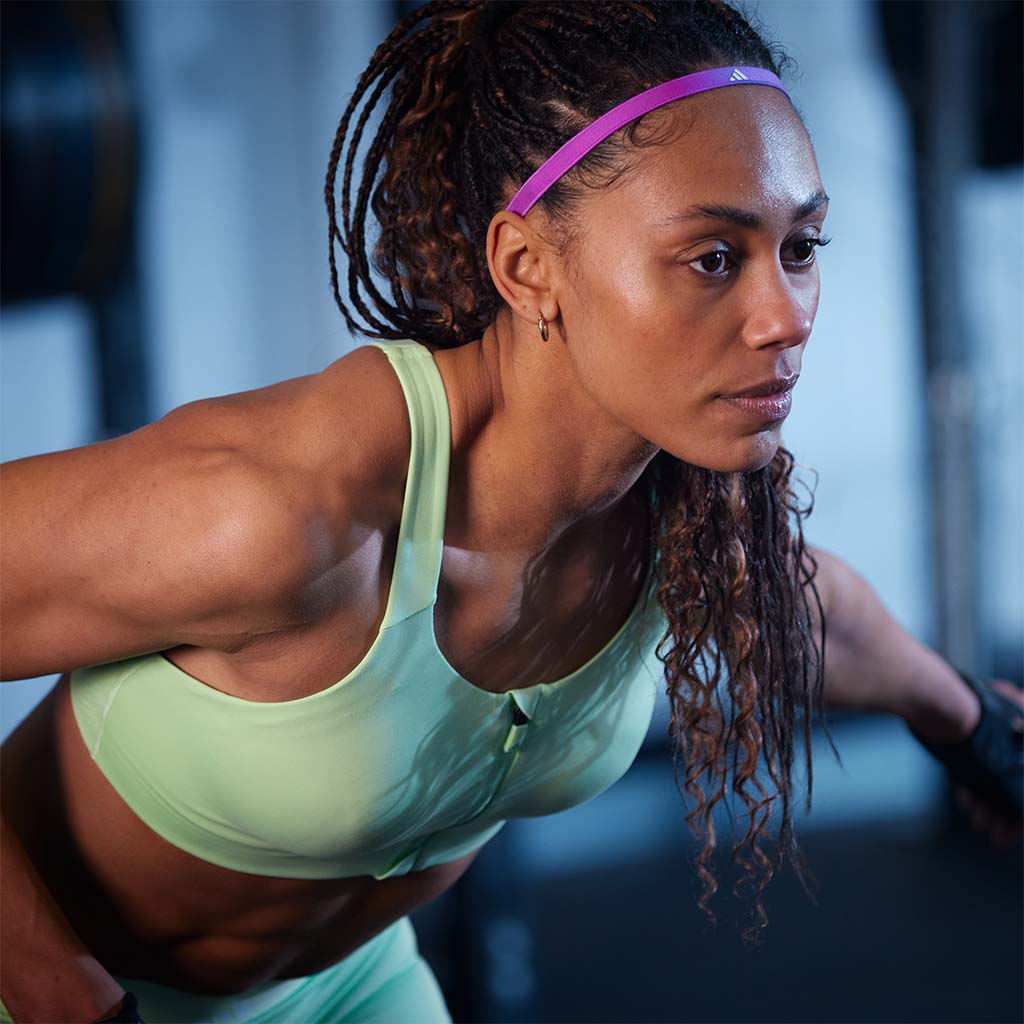 Women in activewear wearing pink adidas headband with a blurry gym in background
