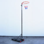 Netball stand against a white wall. Full netball ring system with black steel frame and plastic base. Netball hoop has white red and blue netting.
