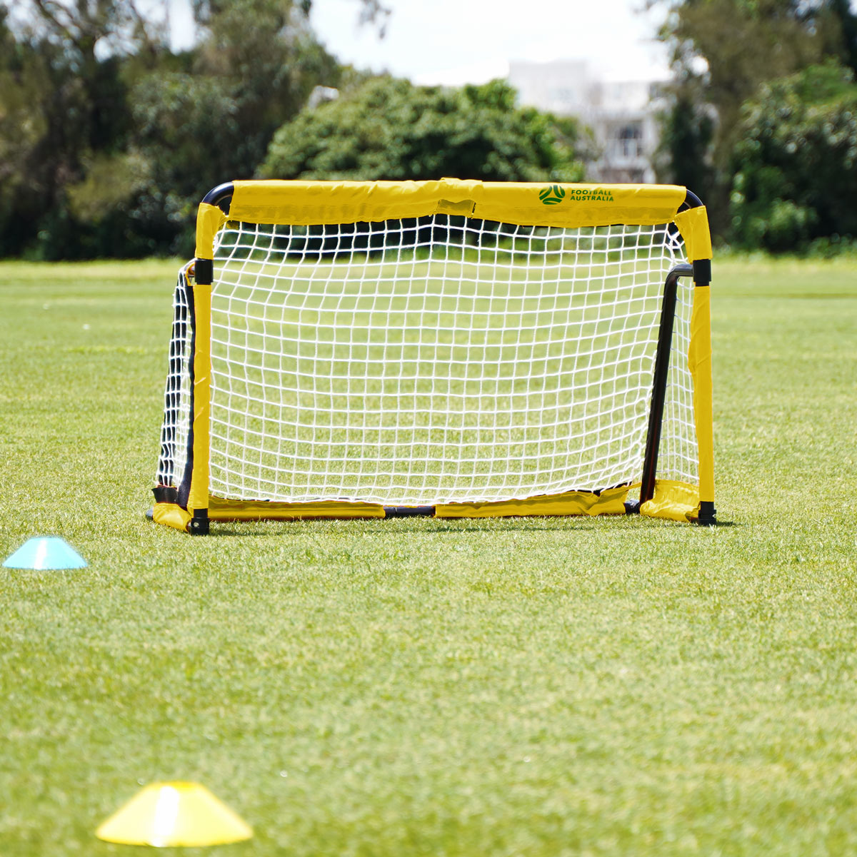 SUMMIT Yellow and black portable soccer goal on a grass field with trees in the background. Ready for training and game on football field. 