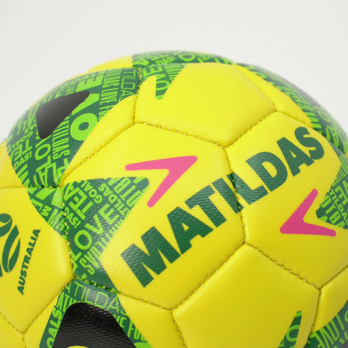 A close-up of a yellow soccer ball with green and black patterns, featuring the brand name 'MATILDAS' in green and pink accents.