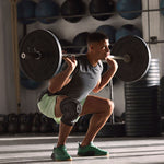 Man doing a squat in a gym with heavy weights, wearing the adidas aeroready knee support