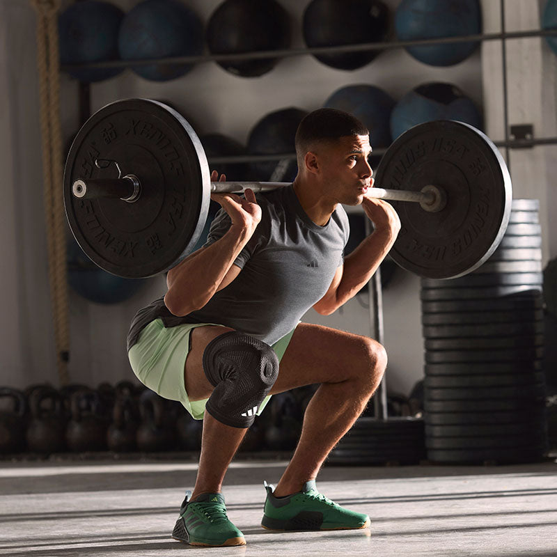 Man doing a squat in a gym with heavy weights, wearing the adidas aeroready knee support