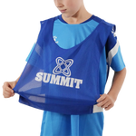 A child wearing a blue Summit athletic training bib over a light blue soccer jersey, holding the bottom of the bib open against a white background.