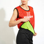 A person wearing a reversible singlet bib with red on one side and fluro green on the other, featuring the Summit logo.