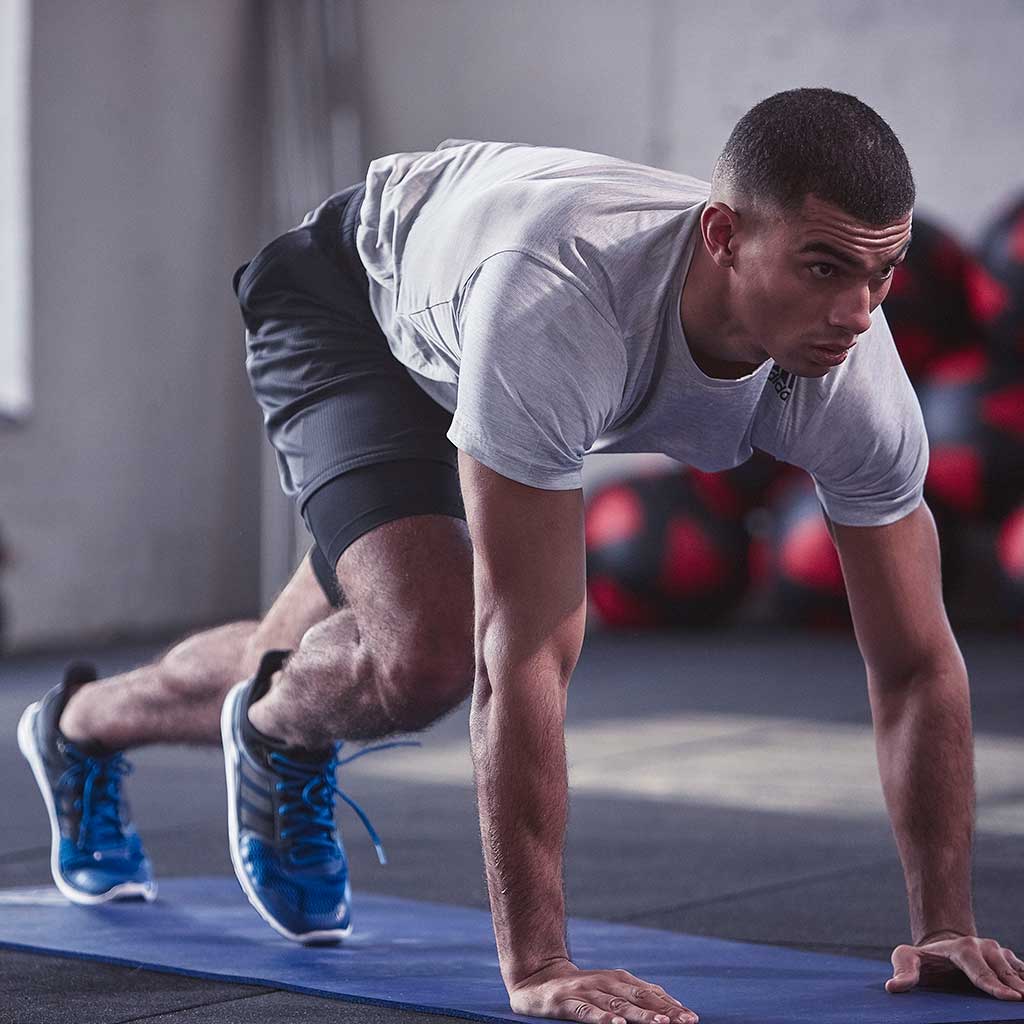 Male uses adidas 7mm fitness mat in blue at the gym to complete his workout on.